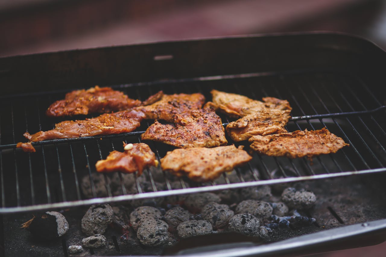 about-us Delicious marinated meats sizzling on a charcoal barbecue grill, perfect for outdoor summer cooking.